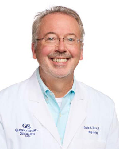 Middle-aged man wearing glasses and a white medical coat, smiling at the camera against a plain white background.